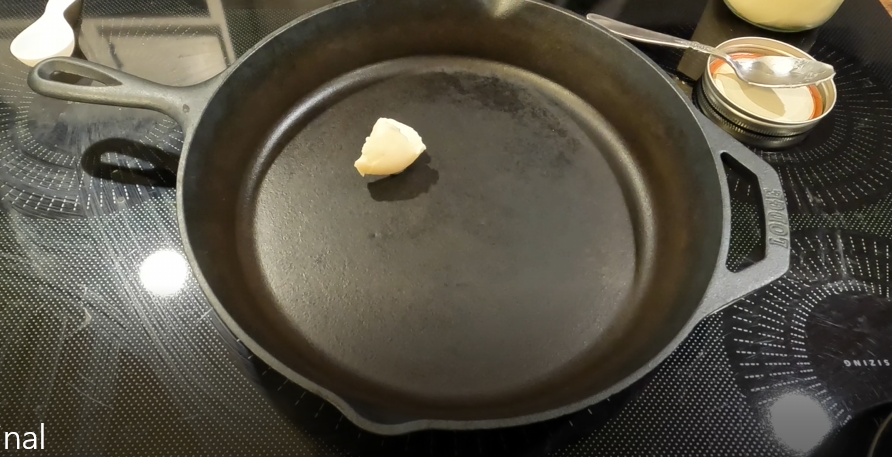 A tablespoon of lard in a cast iron pan on a glass cooktop