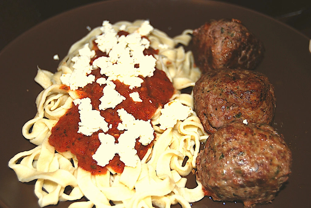 3 meatballs lined up along fettucine pasta topped with sauce and cheese