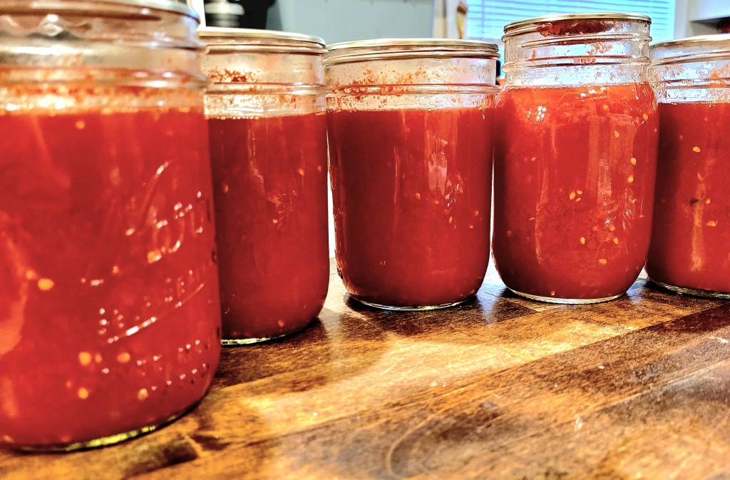 5 half pint jars full of crushed tomatoes on butcher block counter