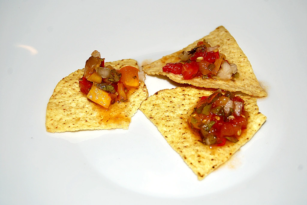 Fermented salsa on 3 tortilla chips on a white plate.