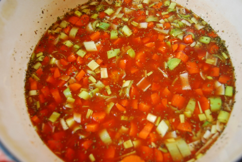 chopped vegetables with broth and seasonings in an enameled cast iron pot