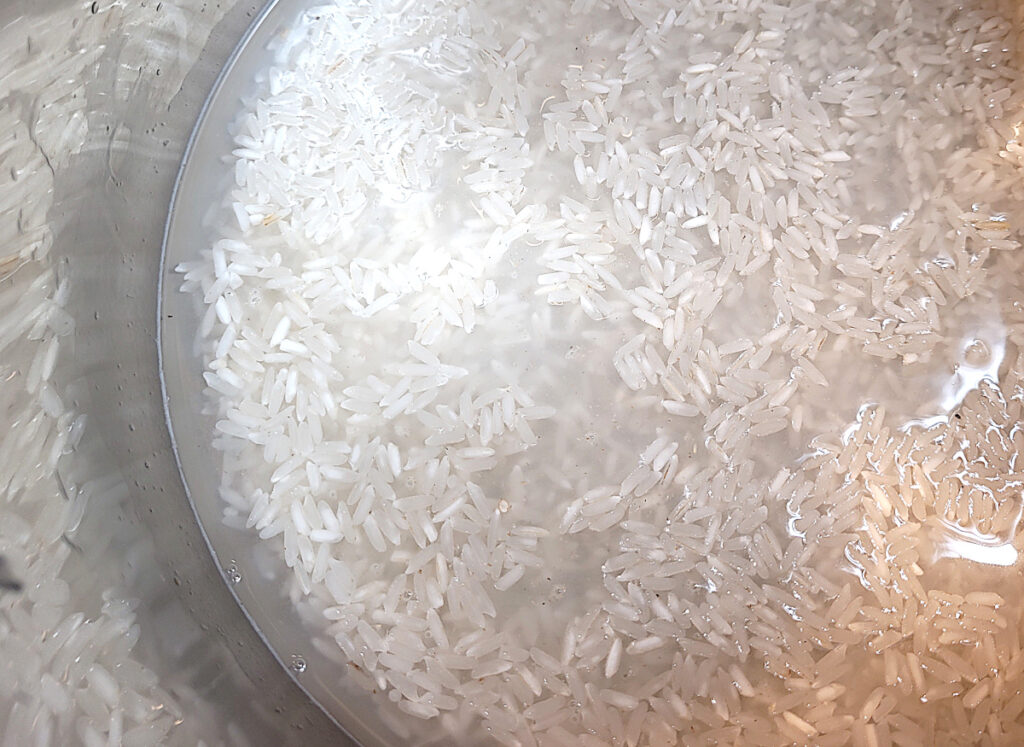 equal amounts of water and long grain rice in a stainless steel bowl