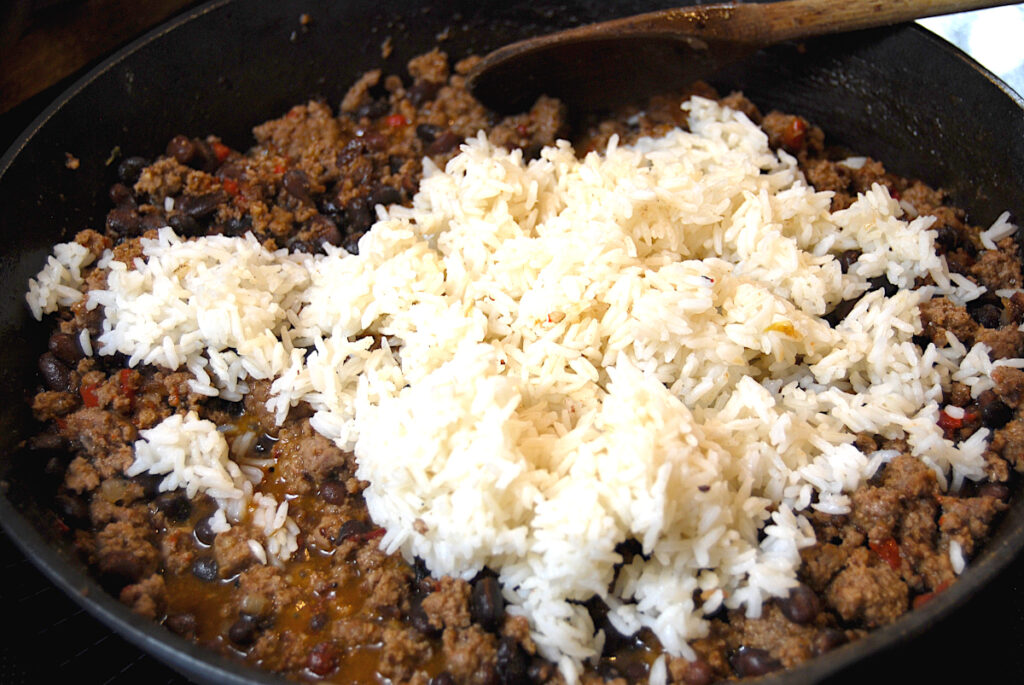 cooked rice added to dirty rice mixture in a cast iron skillet