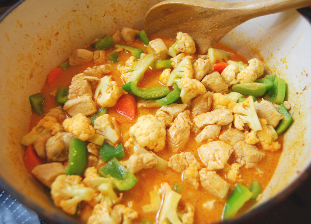 Chopped up cauliflower, green bell peppers, carrots and bite sized chicken in Thai red curry paste and coconut milk