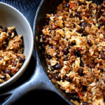gray bowl of dirty rice on the left and a cast iron skillet of dirty rice on the right