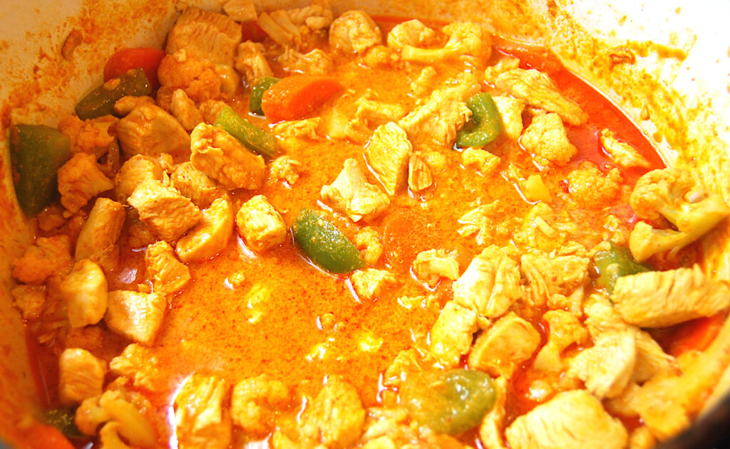 Thai red curry chicken cooking in an enamel coated cast iron pot
