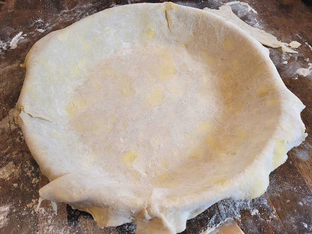 bottom pie crust laid out in pie pan on floured butcherblock counter