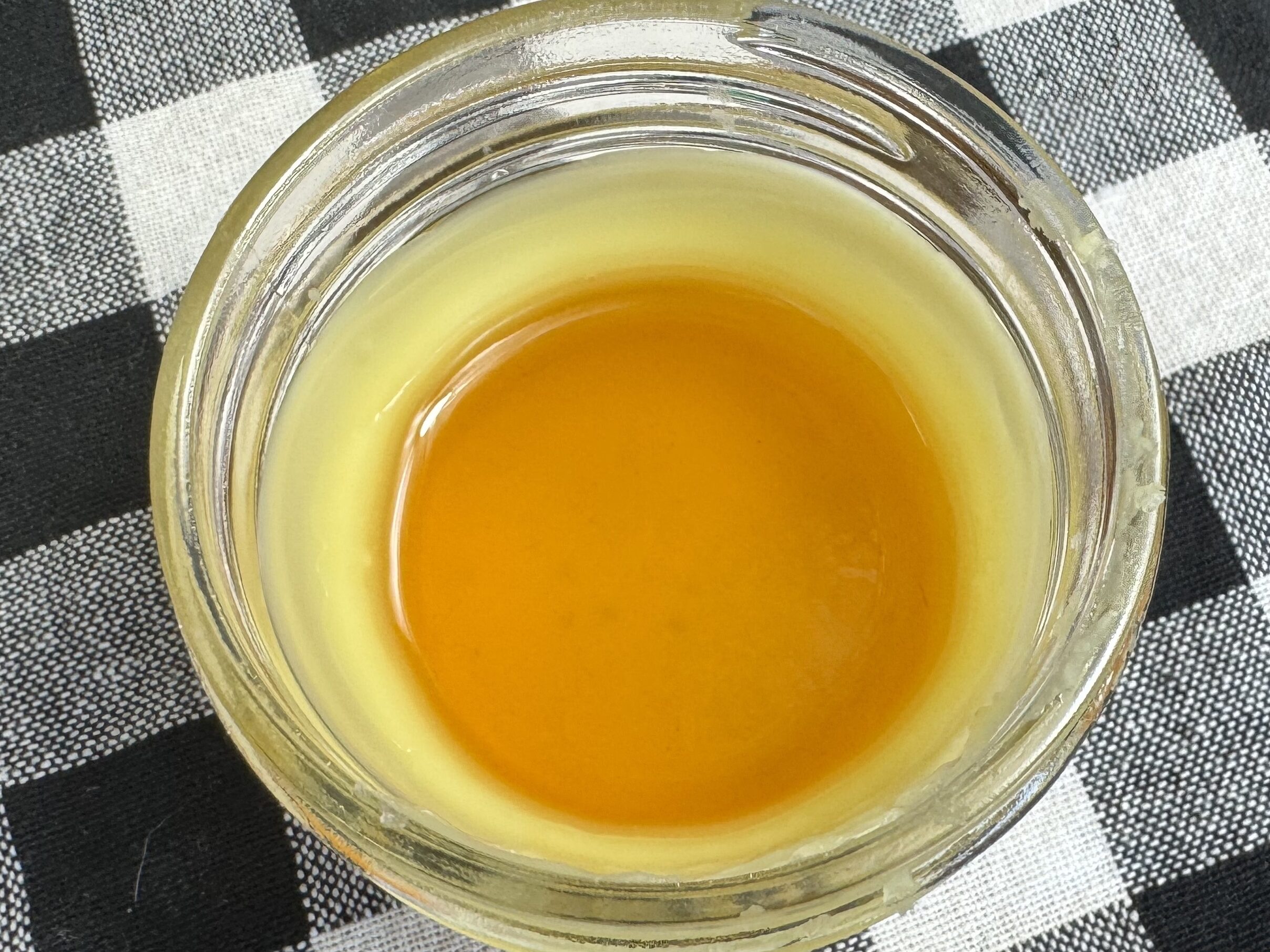 close up of the DIY healing salve in a 4 oz glass jar.  The outer part if solidifying and the inner portion is still liquid.  The glass is sitting on a black and white checkered table cloth