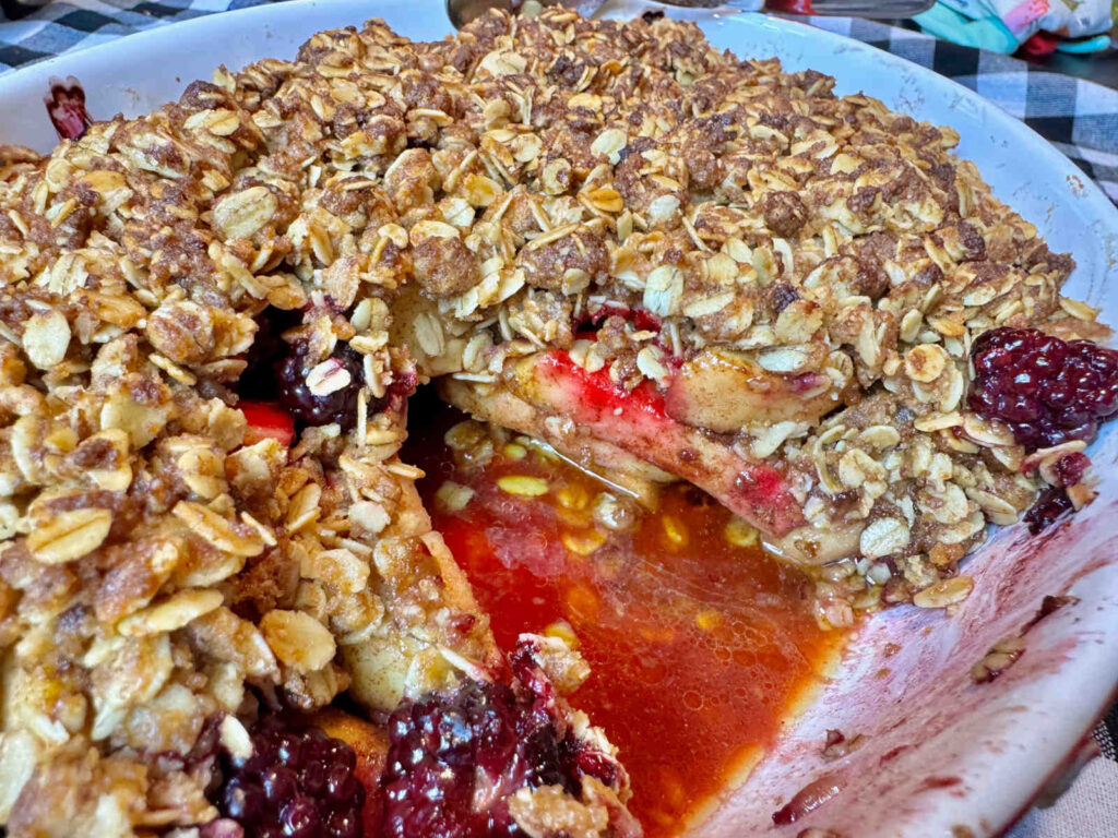 a casserole dish of apple and blackberry crisp with oat topping with a spoonful taken out