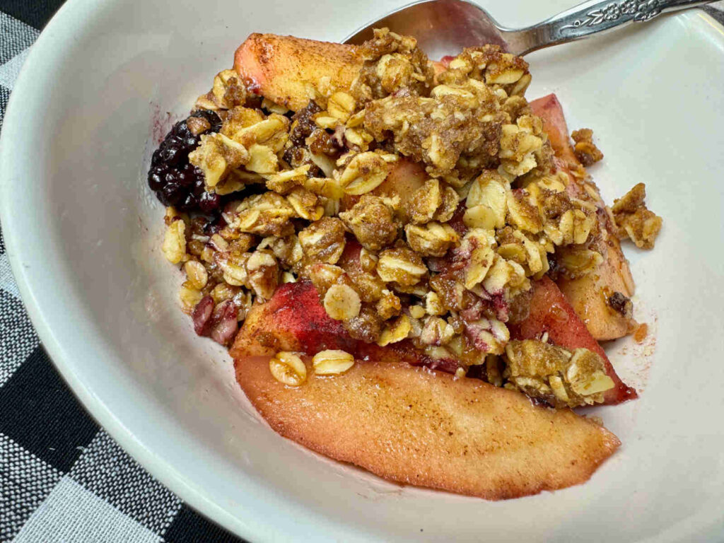 pieces of apple and blackberries topped with an oat topping in a white bowl