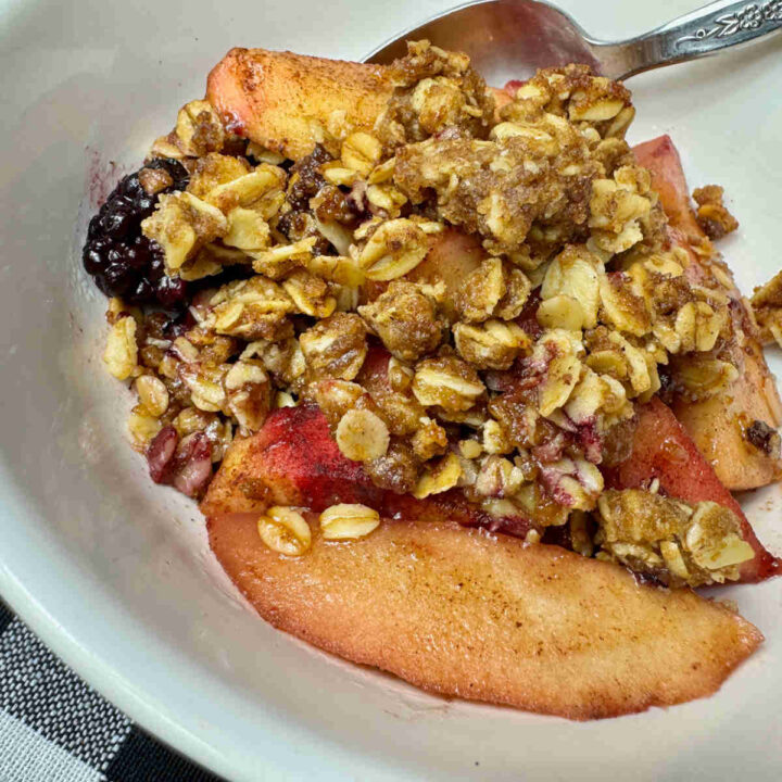 white bowl filled with apple and blackberries with an oat crisp topping