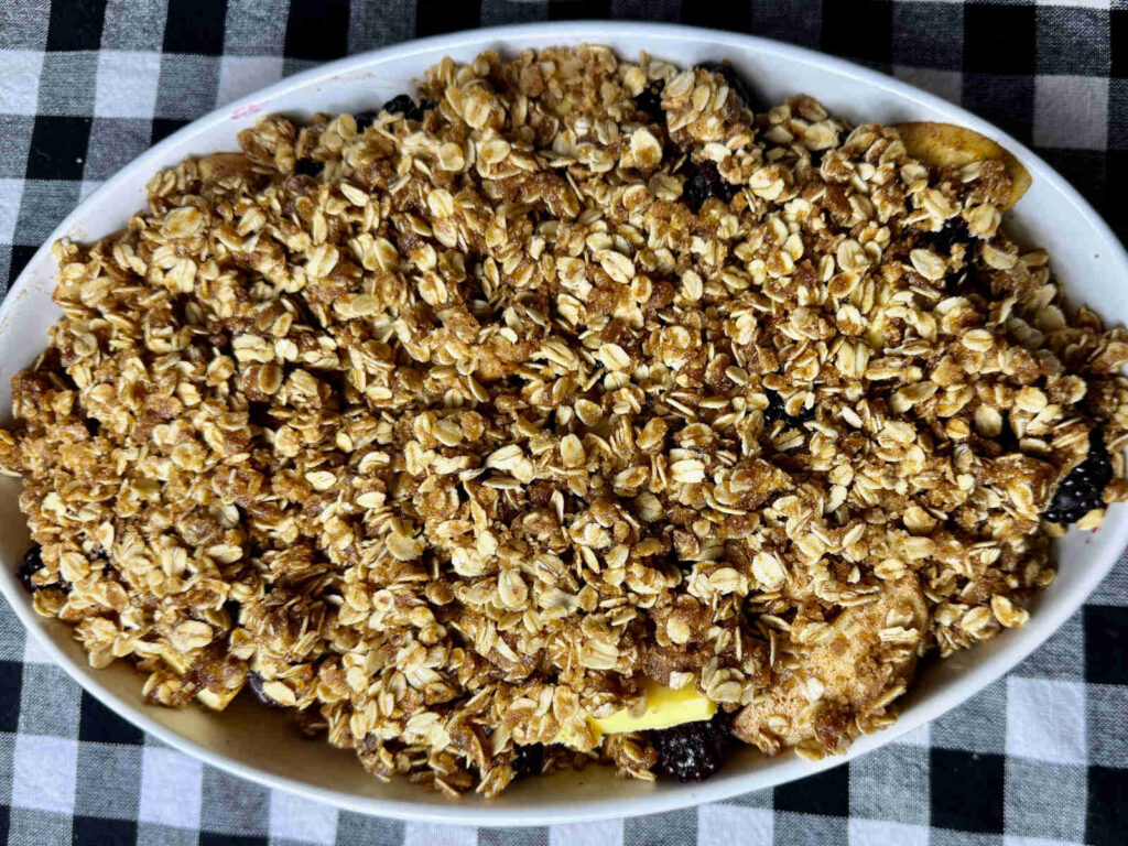 looking down on the unbaked apple and blackberry crisp with oat topping in a white casserole dish on a black and white checkered cloth