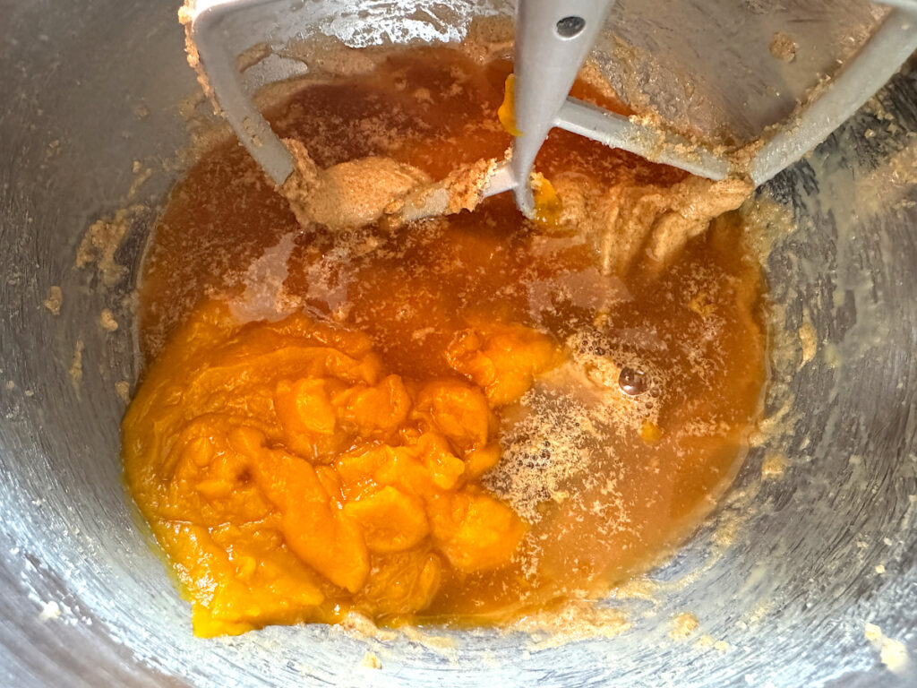 pumpkin and apple cider added to mixture in a stainless steel mixing bowl