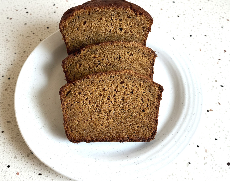 three slices of pumpkin bread with apple cider on a white plate sitting on a light colored granite countertop