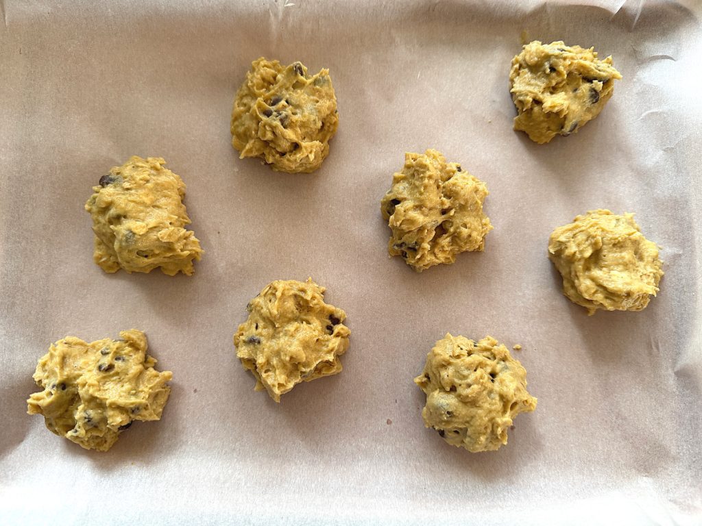 9 tablespoon drops of cookie batter on a parchment paper lined cookie sheet