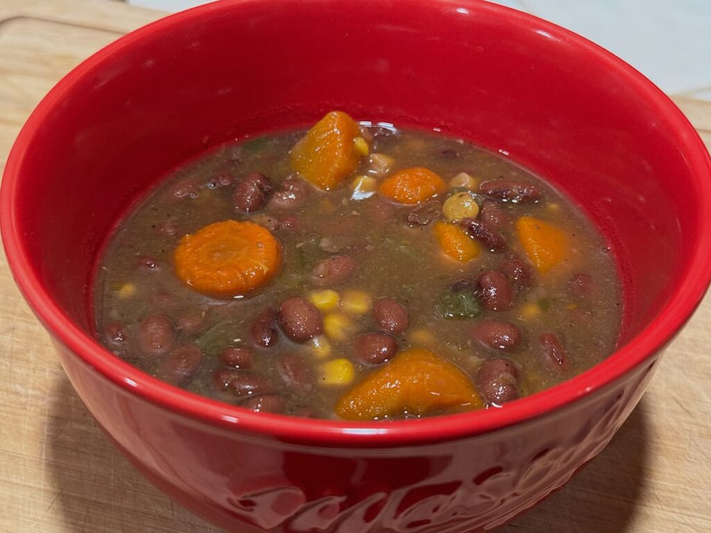 red bowl of black bean soup with carrots and corn