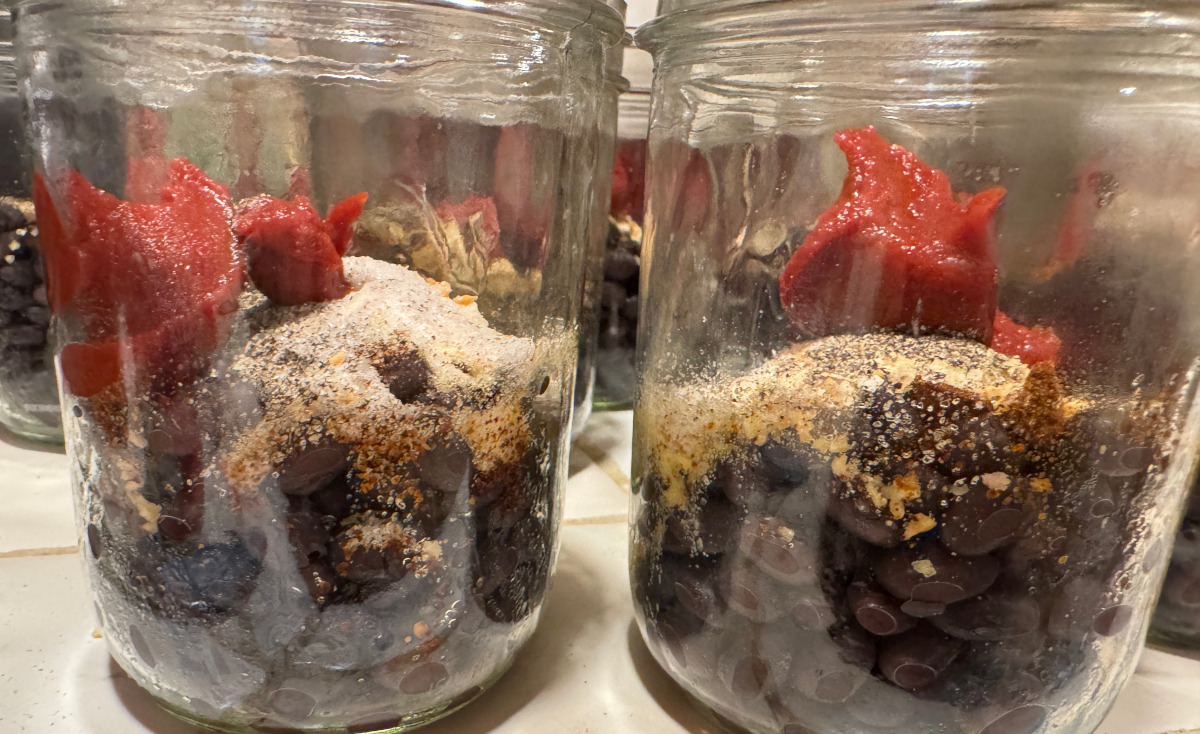 jars half full of black beans with seasonings and tomato paste added