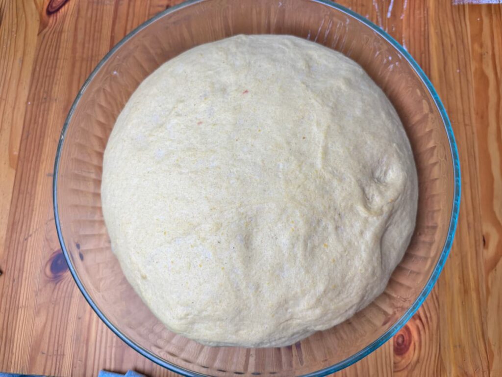 proofed butternut squash bread dough in a glass bowl sitting on a wooden table