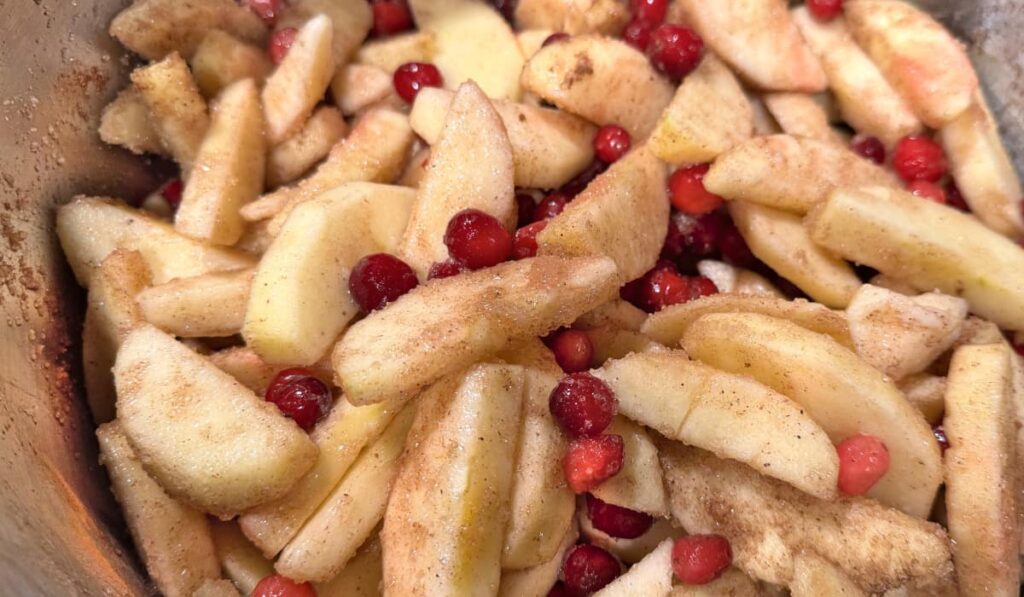 Apple slices and Cranberries mixed with sugar and spices in a stainless steel stock pot