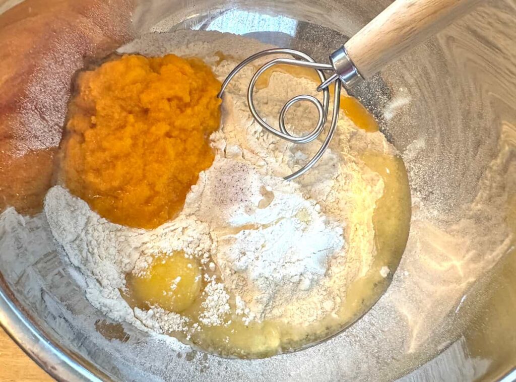 butternut squash dinner roll ingredients in a metal bowl with a dough whisk