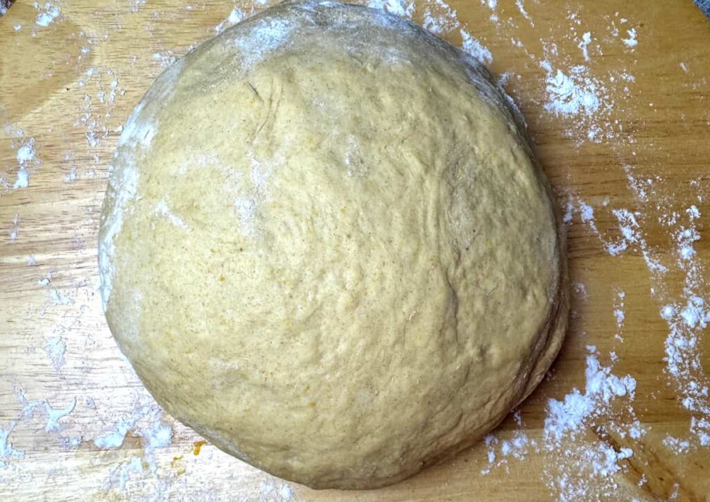 kneaded butternut squash roll dough on a wooden table dusted with flour