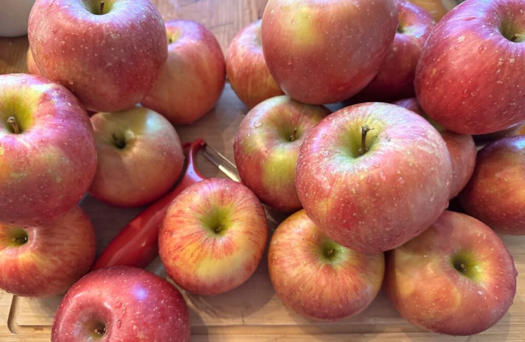 Pile of apples on a wooden cutting board with a red peeler in the middle of them