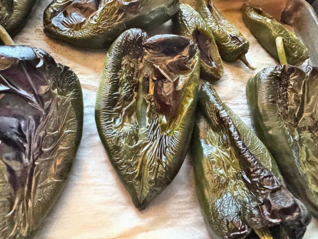 roasted poblano and jalapeno peppers with blistered skin on a parchment lined baking sheet