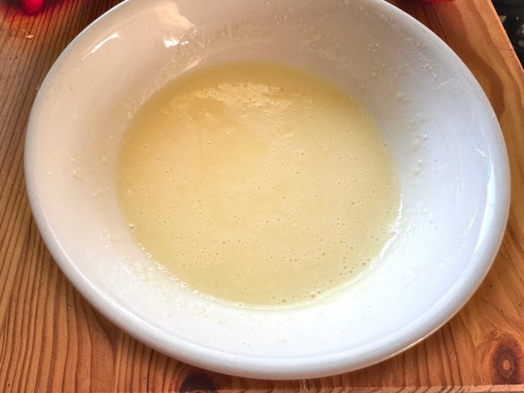 orange icing in a white bowl on a wooden table
