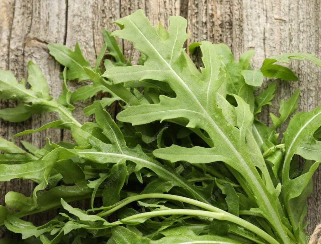 close up of arugula leaves sitting on a piece of light colored wood