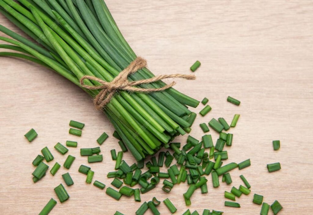 bundle of chives, tied together with a piece of string and diced chives on a wooden background